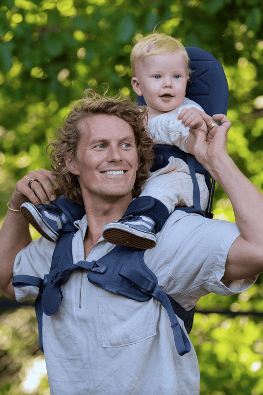 Parent carrying toddler using MiniMeis G4 Shoulder Carrier in navy color.